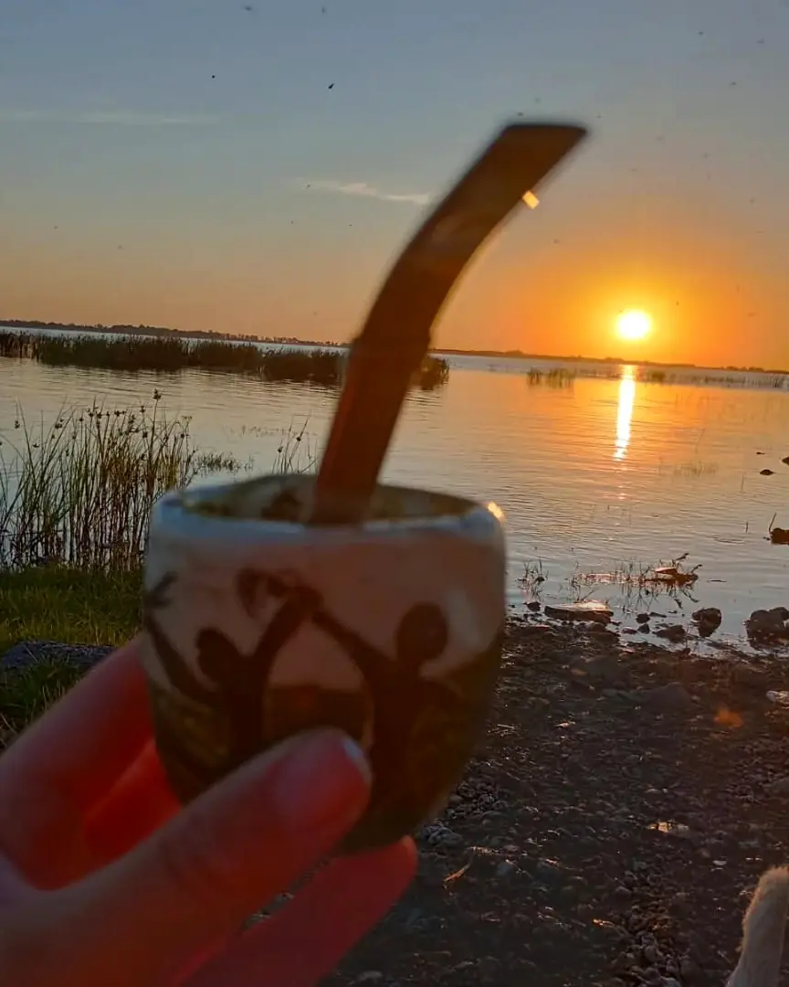 Un mate en la mano frente a la laguna de Chascomús, con el sol poniéndose sobre el agua.