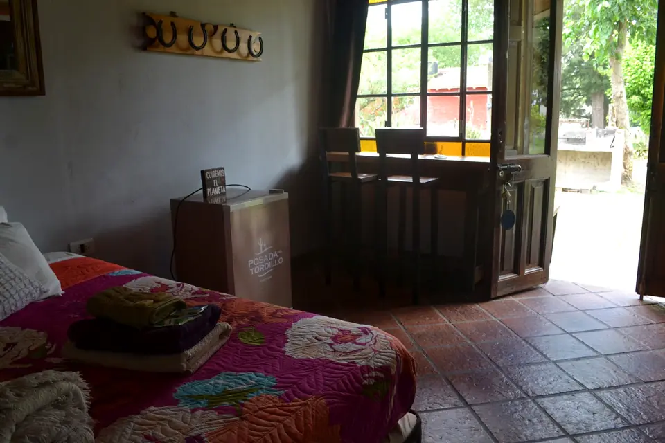 Una habitación con cama de dos plazas y colcha de flores, con la puerta abierta al parque.