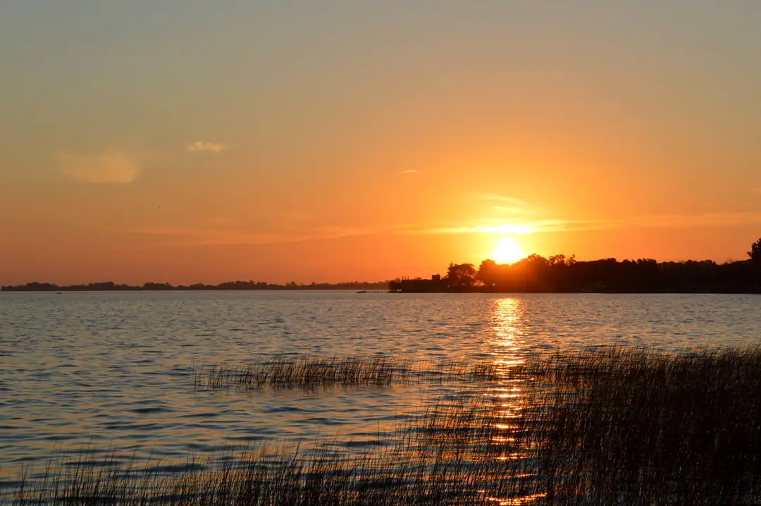 El sol se pone sobre la laguna de Chascomús, con juncos en la orilla.