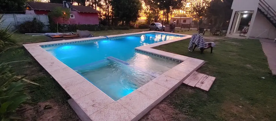 La pileta en L al atardecer, con el parque y la casa blanca al fondo.