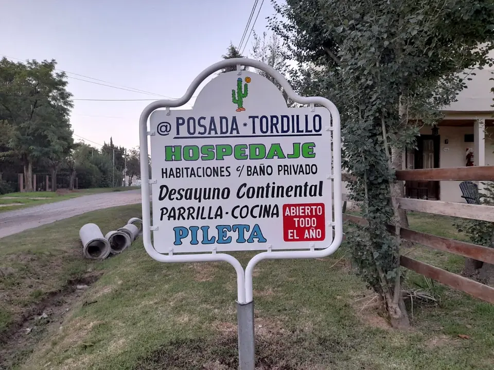El cartel blanco de Posada Tordillo en la vereda, con la casa detrás.